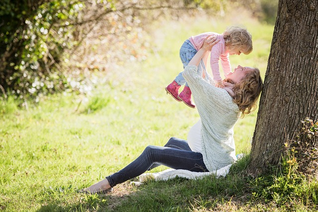 pregnant woman throwing toddler in the air sitting by a tree