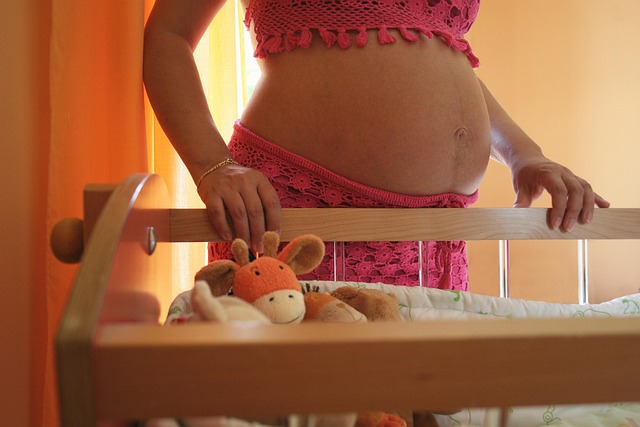 pregnant belly beside baby crib